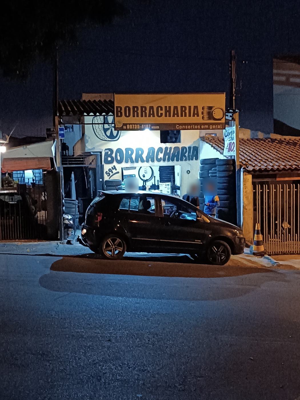 Fachada iluminada da borracharia à noite, com carro estacionado em frente